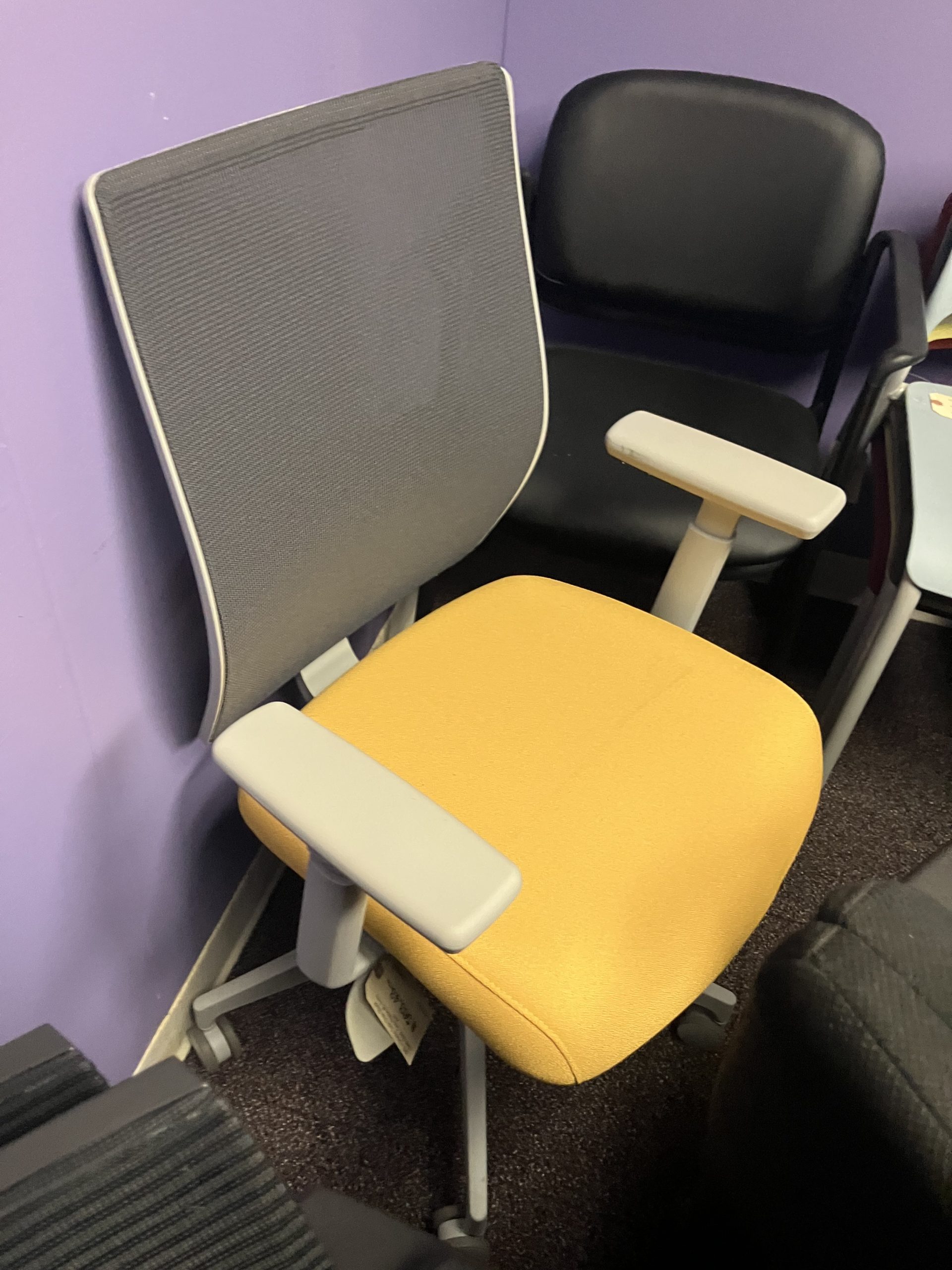 Office chair with a yellow seat and gray backrest against a purple wall at an office.