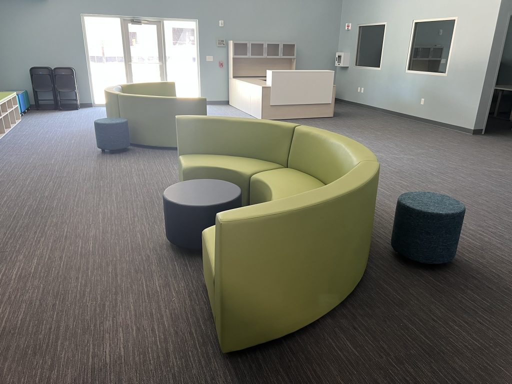 A spacious reception area featuring lime green curved Hon sofas, dark blue cylindrical ottomans, and a central reception desk against a light blue wall.