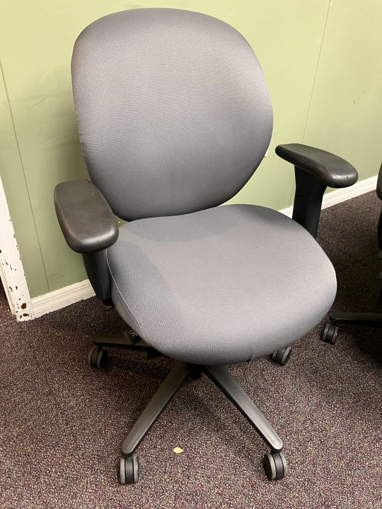 Gray office chair with padded back and armrests on a black pedestal base, placed on a speckled carpet by a light-green wall.