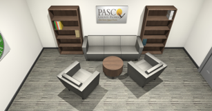A small modern waiting room with two beige armchairs around a round wooden coffee table, a gray sofa against the back wall, tall wooden bookshelves on either side, and a PASCO sign on the wall.
